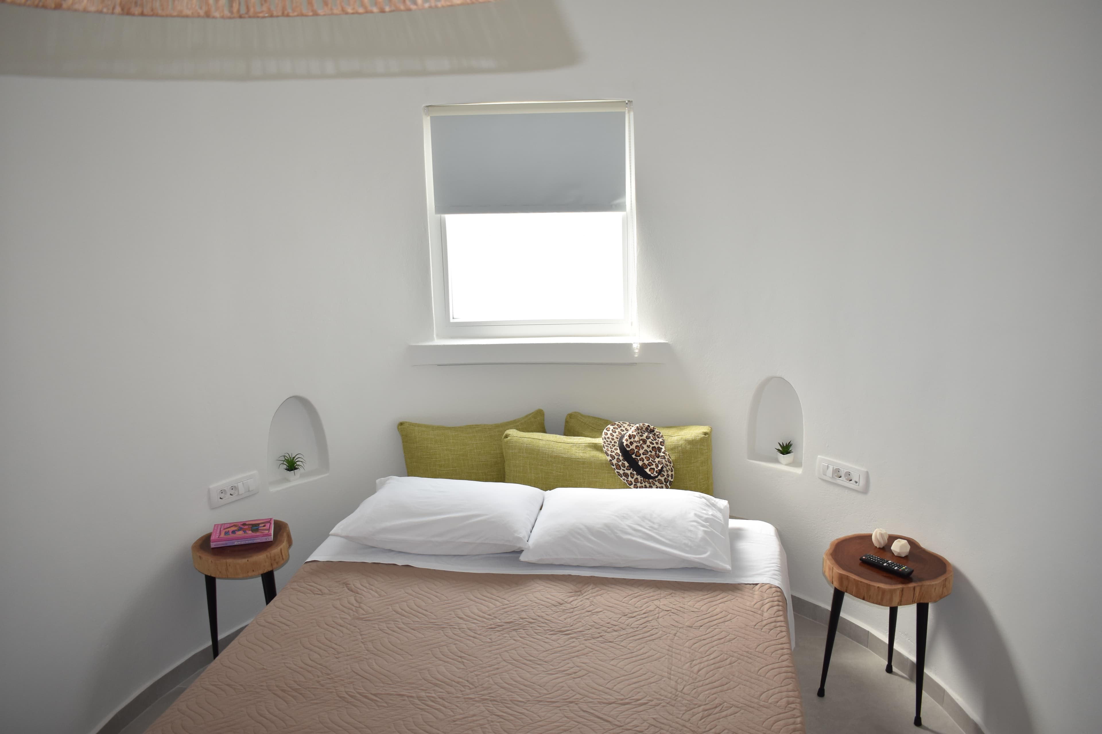Minimalist bedroom with curved white walls, bed with green pillows, leopard hat, and side tables.